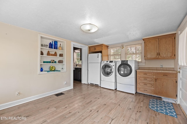 washroom with cabinets, light wood-type flooring, a textured ceiling, built in shelves, and independent washer and dryer