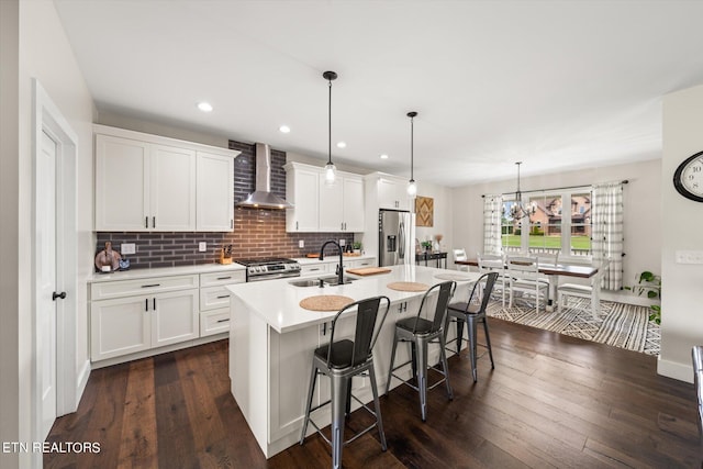 kitchen featuring an island with sink, sink, dark hardwood / wood-style floors, wall chimney exhaust hood, and appliances with stainless steel finishes