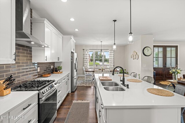 kitchen featuring white cabinets, stainless steel appliances, sink, wall chimney exhaust hood, and a kitchen island with sink