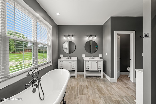 bathroom featuring hardwood / wood-style floors, a tub to relax in, toilet, and vanity