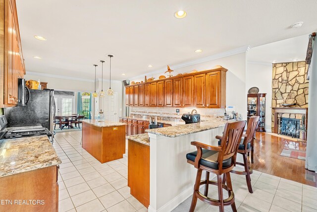 kitchen featuring light wood-type flooring, kitchen peninsula, a center island, light stone countertops, and appliances with stainless steel finishes