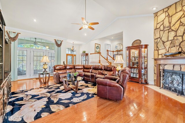 living room featuring vaulted ceiling, light hardwood / wood-style flooring, a stone fireplace, crown molding, and ceiling fan