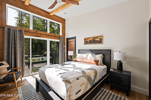 bedroom with beamed ceiling, a high ceiling, access to exterior, ceiling fan, and hardwood / wood-style flooring