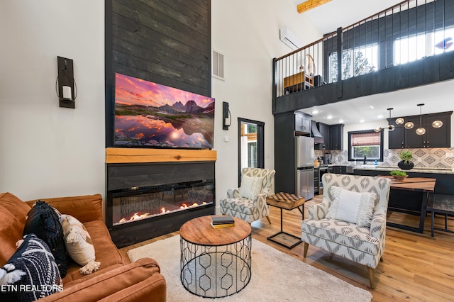 living room with a fireplace, light wood-type flooring, sink, a towering ceiling, and an AC wall unit