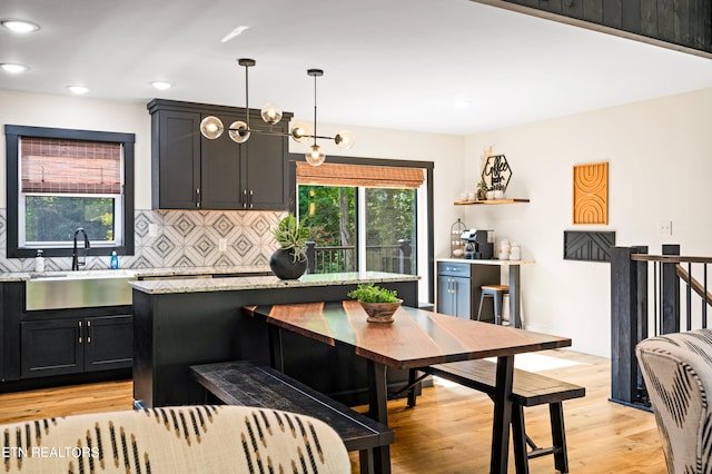 kitchen featuring light wood-type flooring, decorative light fixtures, an inviting chandelier, sink, and decorative backsplash