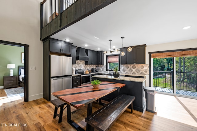 kitchen featuring stainless steel appliances, decorative light fixtures, plenty of natural light, light stone countertops, and custom range hood