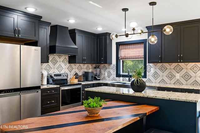 kitchen featuring light stone counters, decorative backsplash, hanging light fixtures, appliances with stainless steel finishes, and custom range hood