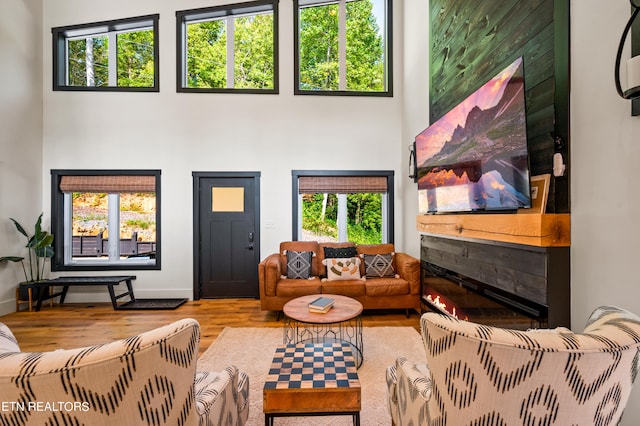 living room with a high ceiling, a tiled fireplace, and hardwood / wood-style flooring