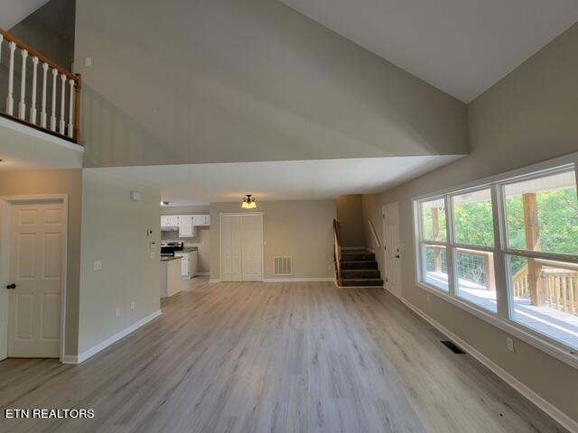 unfurnished living room with light wood-type flooring and high vaulted ceiling