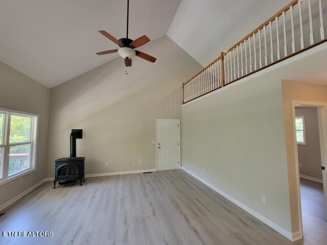 unfurnished living room featuring high vaulted ceiling, ceiling fan, a wood stove, and wood-type flooring