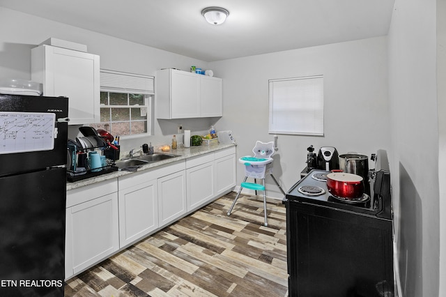 kitchen featuring light stone counters, sink, white cabinetry, black appliances, and light wood-type flooring