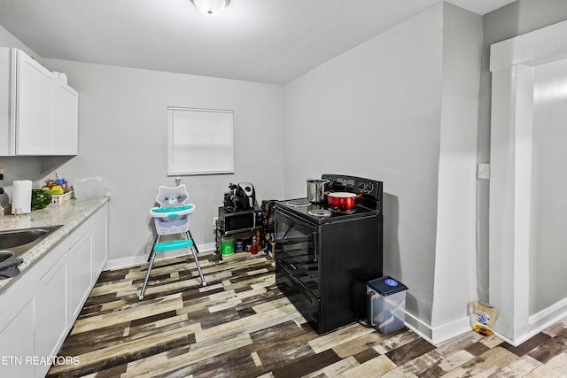 kitchen featuring light wood-type flooring, light stone countertops, white cabinetry, and black electric range