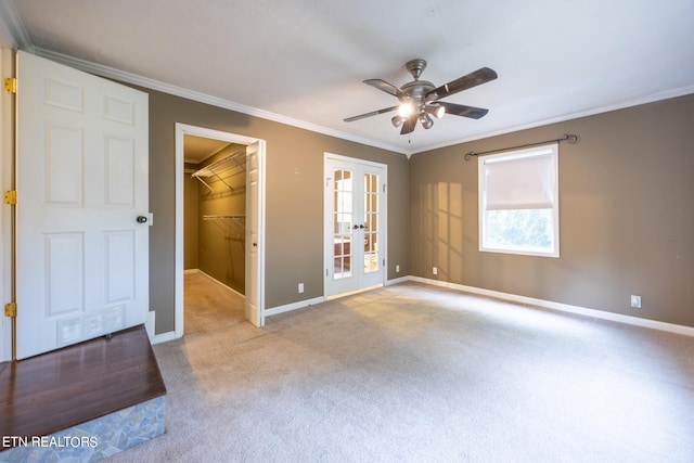 unfurnished bedroom with light carpet, crown molding, ceiling fan, french doors, and a spacious closet