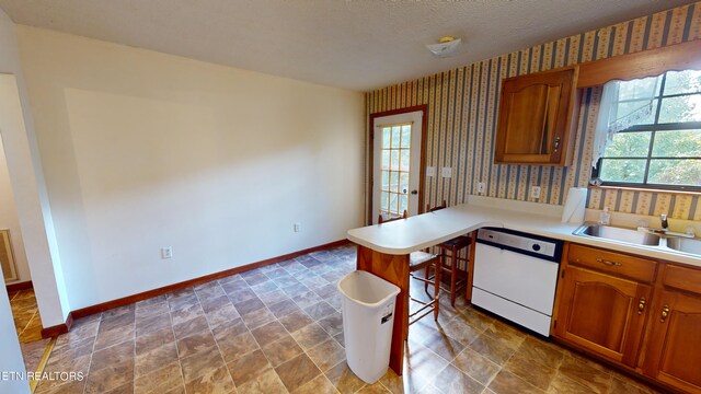 kitchen featuring a textured ceiling, dishwasher, kitchen peninsula, and sink