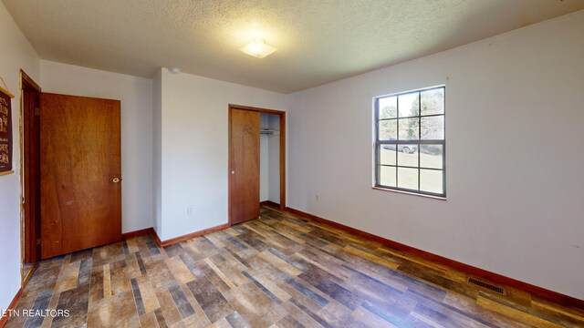 unfurnished bedroom with a textured ceiling, a closet, and dark hardwood / wood-style flooring