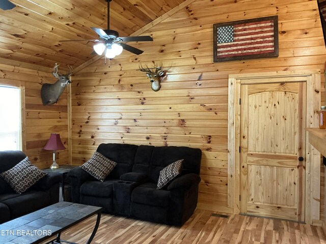 living room with light wood-type flooring, ceiling fan, wooden ceiling, wooden walls, and high vaulted ceiling