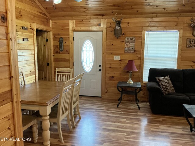 dining room with wooden walls, lofted ceiling, and light hardwood / wood-style floors