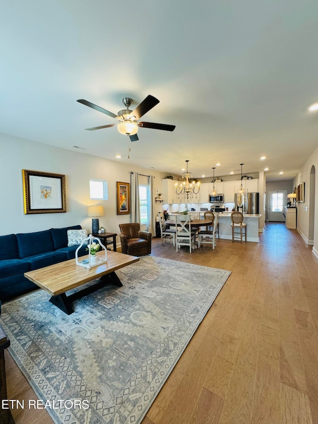 living room with ceiling fan with notable chandelier and light wood-type flooring