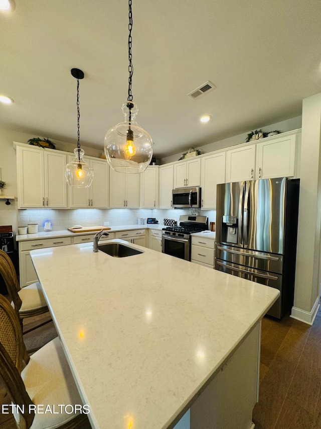 kitchen featuring pendant lighting, white cabinets, sink, an island with sink, and stainless steel appliances