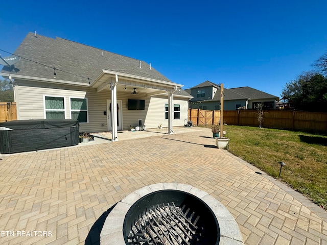 back of property with ceiling fan, a yard, an outdoor fire pit, a hot tub, and a patio