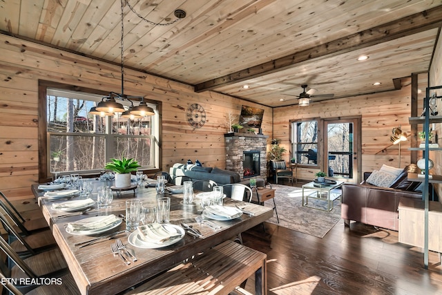 dining area featuring dark wood-type flooring, a healthy amount of sunlight, wood ceiling, and a stone fireplace