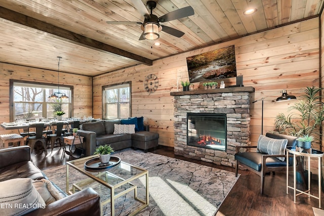 living room featuring hardwood / wood-style flooring, wooden ceiling, a stone fireplace, ceiling fan, and beam ceiling