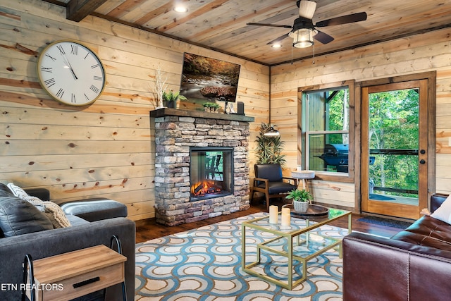 living room with wood walls, wood-type flooring, ceiling fan, a stone fireplace, and wood ceiling