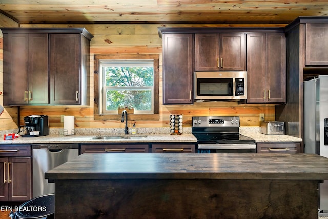 kitchen with dark brown cabinets, appliances with stainless steel finishes, sink, wooden counters, and wooden walls