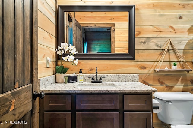 bathroom with vanity, toilet, and wood walls