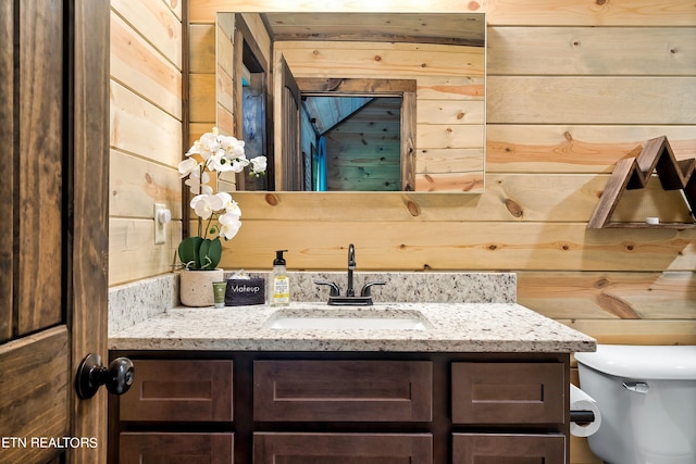 bathroom featuring wood walls, toilet, and vanity