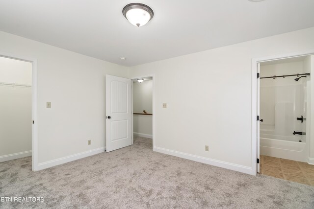 unfurnished bedroom featuring connected bathroom, a spacious closet, light colored carpet, and a closet