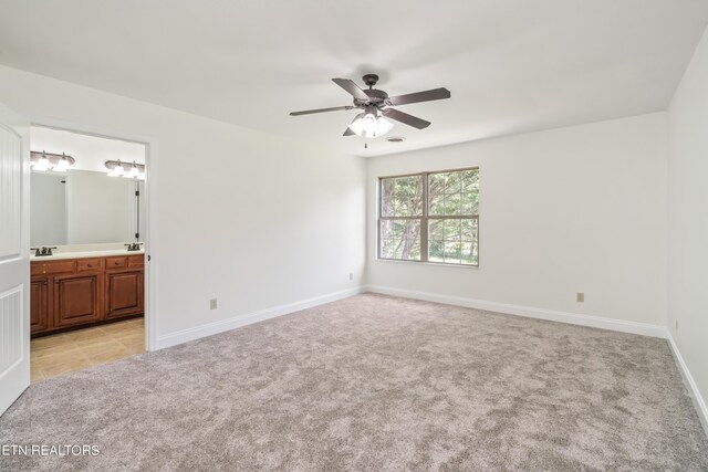 unfurnished bedroom featuring sink, light colored carpet, ensuite bathroom, and ceiling fan