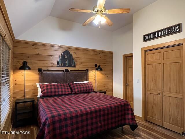 bedroom featuring wood-type flooring, lofted ceiling, ceiling fan, and wooden walls