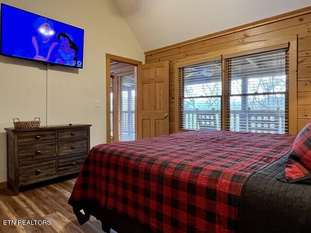 bedroom with wood-type flooring, lofted ceiling, and wood walls