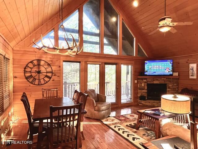 living room featuring ceiling fan with notable chandelier, wooden ceiling, hardwood / wood-style flooring, and a stone fireplace