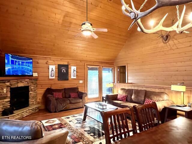 living room featuring ceiling fan, wood-type flooring, wooden walls, high vaulted ceiling, and a fireplace