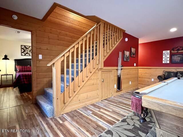 staircase with pool table, wood walls, and hardwood / wood-style flooring