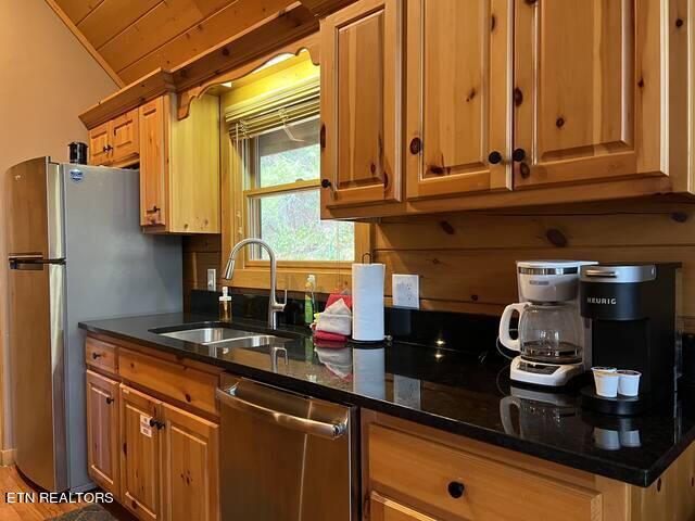 kitchen with appliances with stainless steel finishes, wood ceiling, sink, and dark stone counters