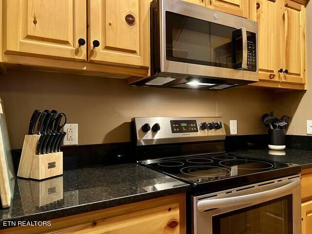 kitchen with dark stone countertops, light brown cabinetry, and stainless steel appliances