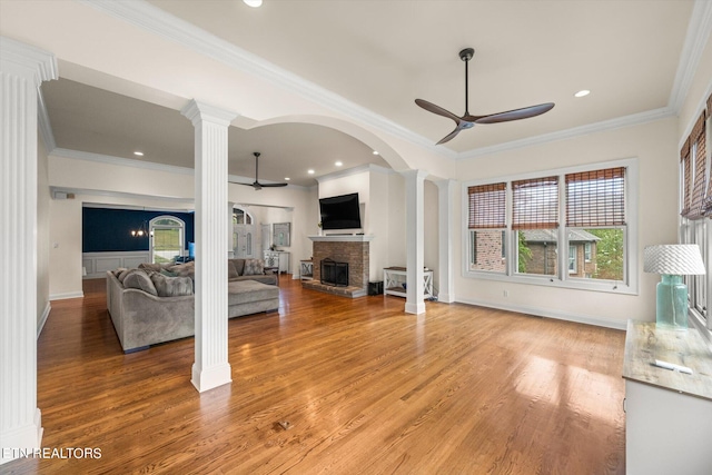 living room with ceiling fan, ornamental molding, wood-type flooring, decorative columns, and a fireplace