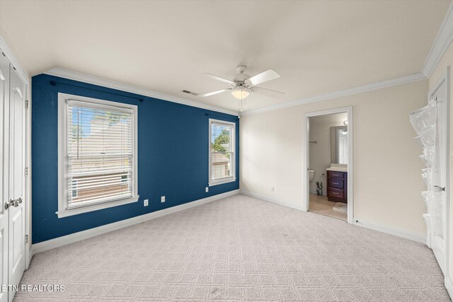 unfurnished bedroom featuring multiple windows, ornamental molding, light carpet, and ensuite bathroom