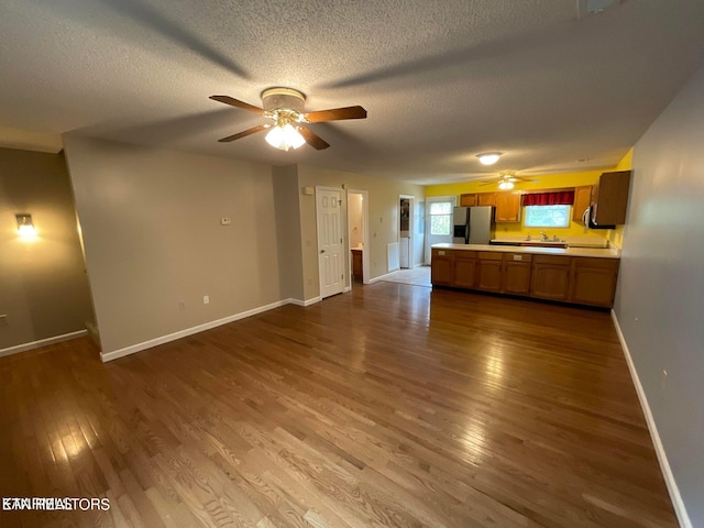 unfurnished living room with a textured ceiling, wood-type flooring, sink, and ceiling fan