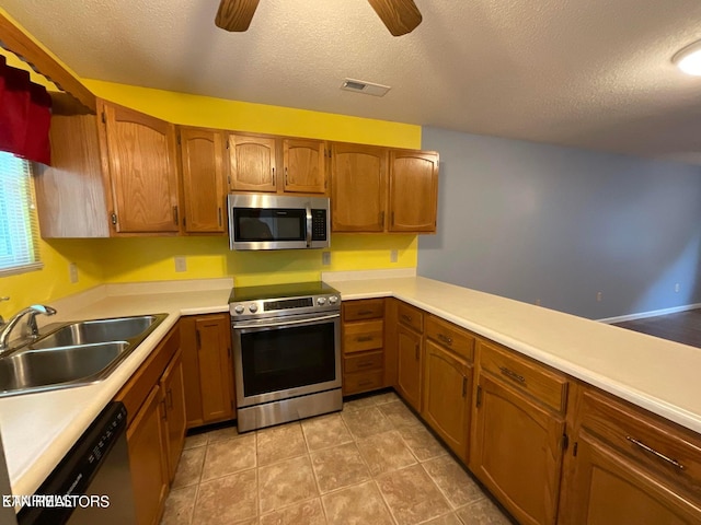 kitchen with stainless steel appliances, sink, kitchen peninsula, ceiling fan, and a textured ceiling