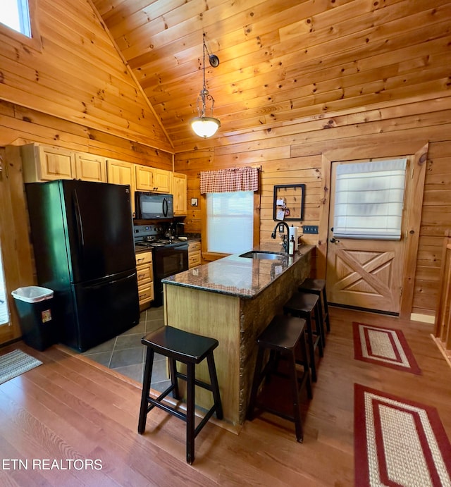 kitchen with light wood-type flooring, pendant lighting, black appliances, sink, and a breakfast bar