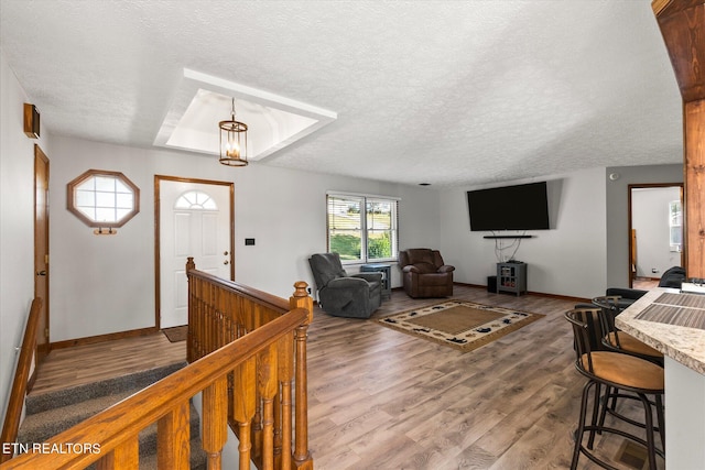 living room with a textured ceiling, a notable chandelier, hardwood / wood-style floors, and a tray ceiling