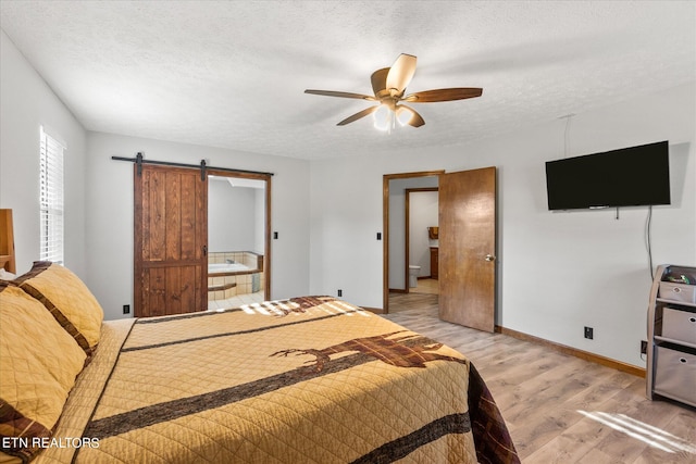 bedroom featuring a textured ceiling, a barn door, ceiling fan, and light hardwood / wood-style floors