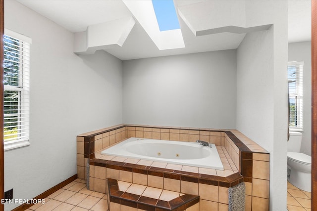 bathroom with a skylight, toilet, a relaxing tiled tub, and tile patterned floors