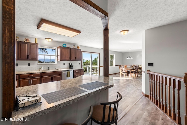 kitchen featuring a textured ceiling, stainless steel dishwasher, decorative light fixtures, and light hardwood / wood-style floors