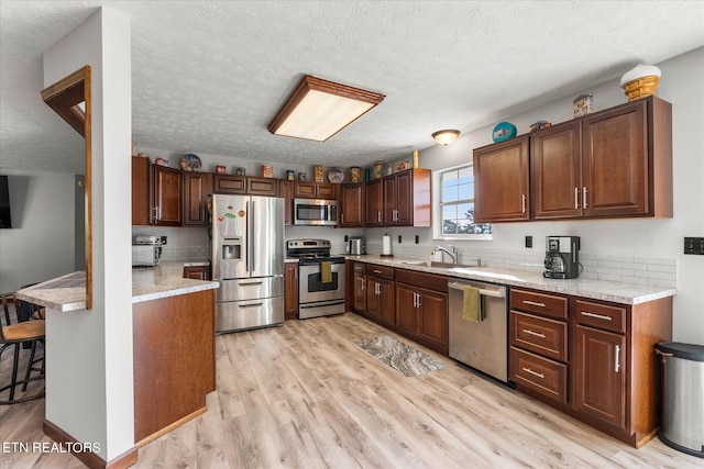 kitchen featuring a textured ceiling, a kitchen breakfast bar, light hardwood / wood-style floors, stainless steel appliances, and sink