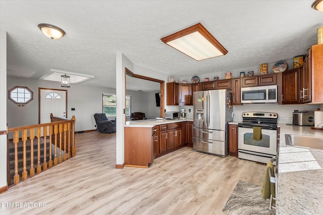 kitchen with a textured ceiling, light wood-type flooring, sink, and appliances with stainless steel finishes